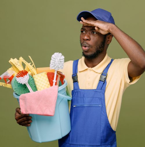 surprised holding bucket of cleaning tools young africanamerican cleaner male in uniform with gloves isolated on green background